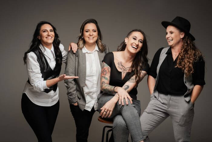 Le Farfalle Quatro mulheres sorrindo em frente à parede cinza