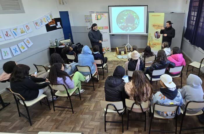 Projeto leva o ritmo do bugio de volta às escolas Homens palestrando sobre música em sala de aula