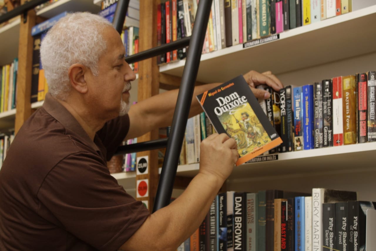 Homem em escada colocando livro na prateleira