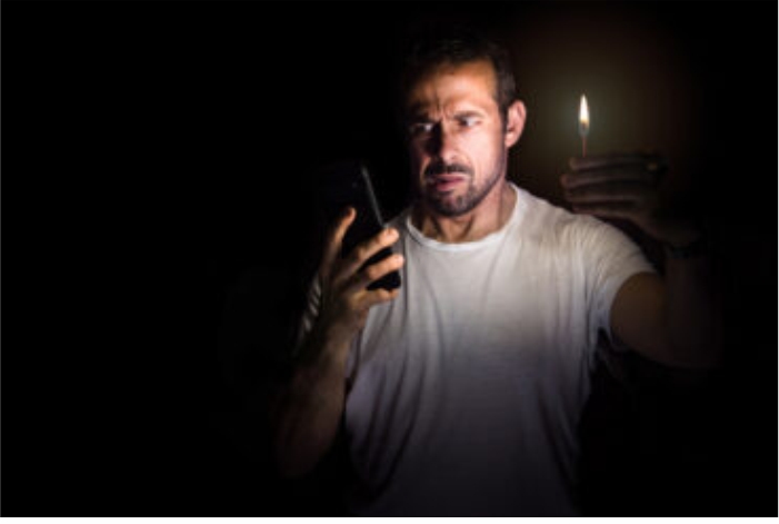 Homem desconfiado olhando para o celular e segurando um fósforo em ambiente escuro