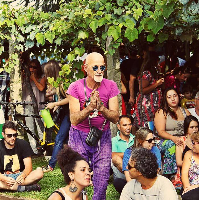 Claudio Troian com roupas cor-de-rosa e câmera pendurada no pescoço em meio a pessoas ao ar livre