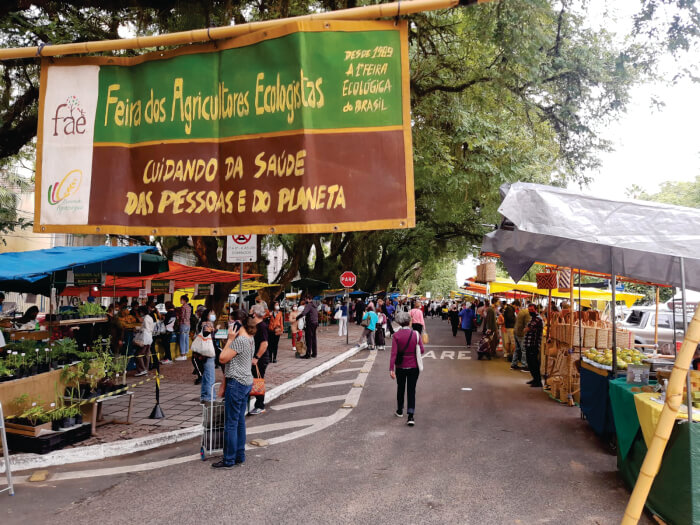 Pessoas embaixo de placa da Feira dos Agricultores Ecologistas