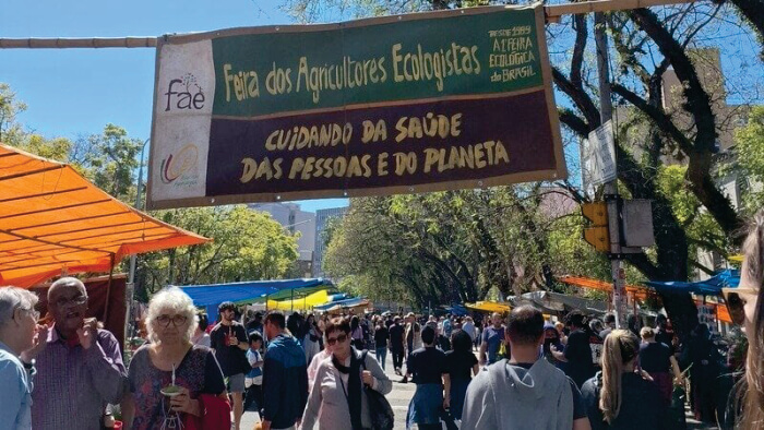 Pessoas embaixo de placa da Feira dos Agricultores Ecologistas