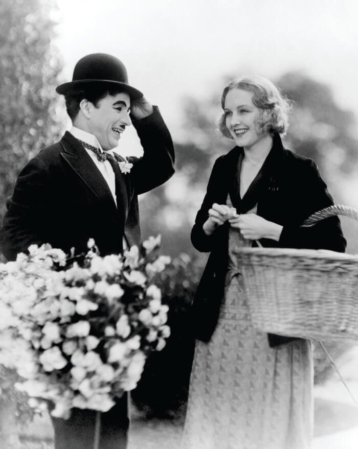 Charlie Chaplin segurando flores ao lado de uma mulher segurando cesta