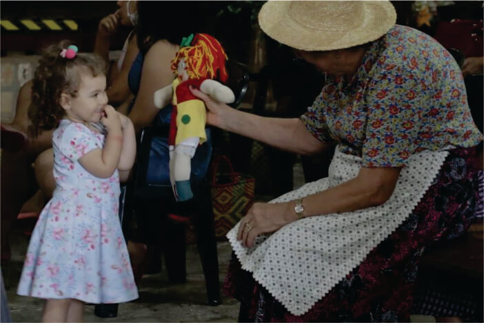 Senhora entregando boneca da Emília para criança