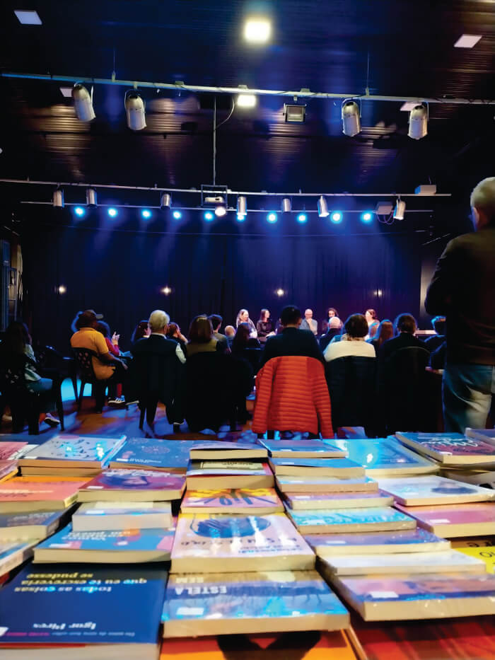 Bancada com livros atrás de pessoas sentadas olhando para o palco