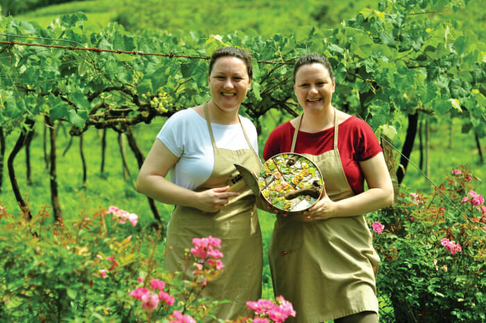 Duas mulheres sorrindo em jardim enquanto seguram peça de arte