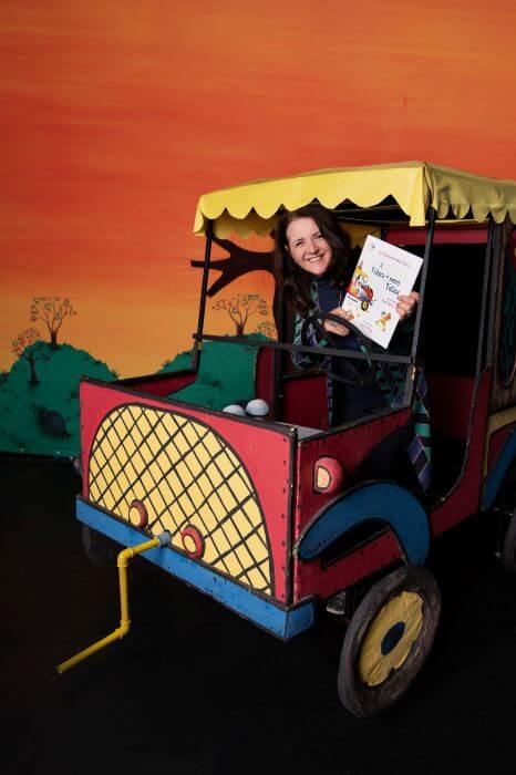 Mulher em veículo cenográfico segurando livro
